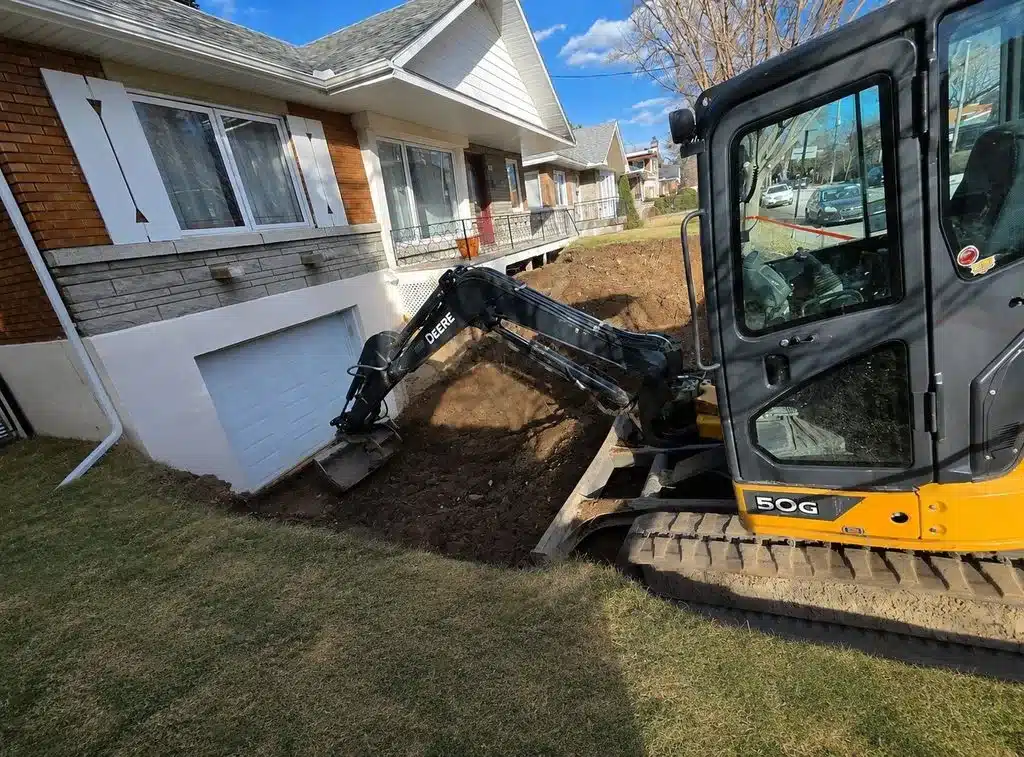 Mini-pelle excavant le terrain devant une maison résidentielle.