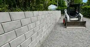 Mur de soutènement en blocs de béton nouvellement construit le long d’une allée en gravier.