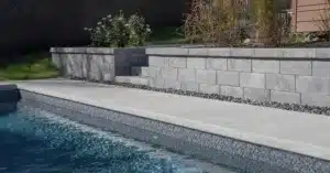 Murets paysagers en blocs de béton gris avec marches intégrées, aménagés au bord d’une piscine creusée.
