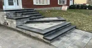 Escalier extérieur rénové en blocs de béton gris avec marches noires et palier.